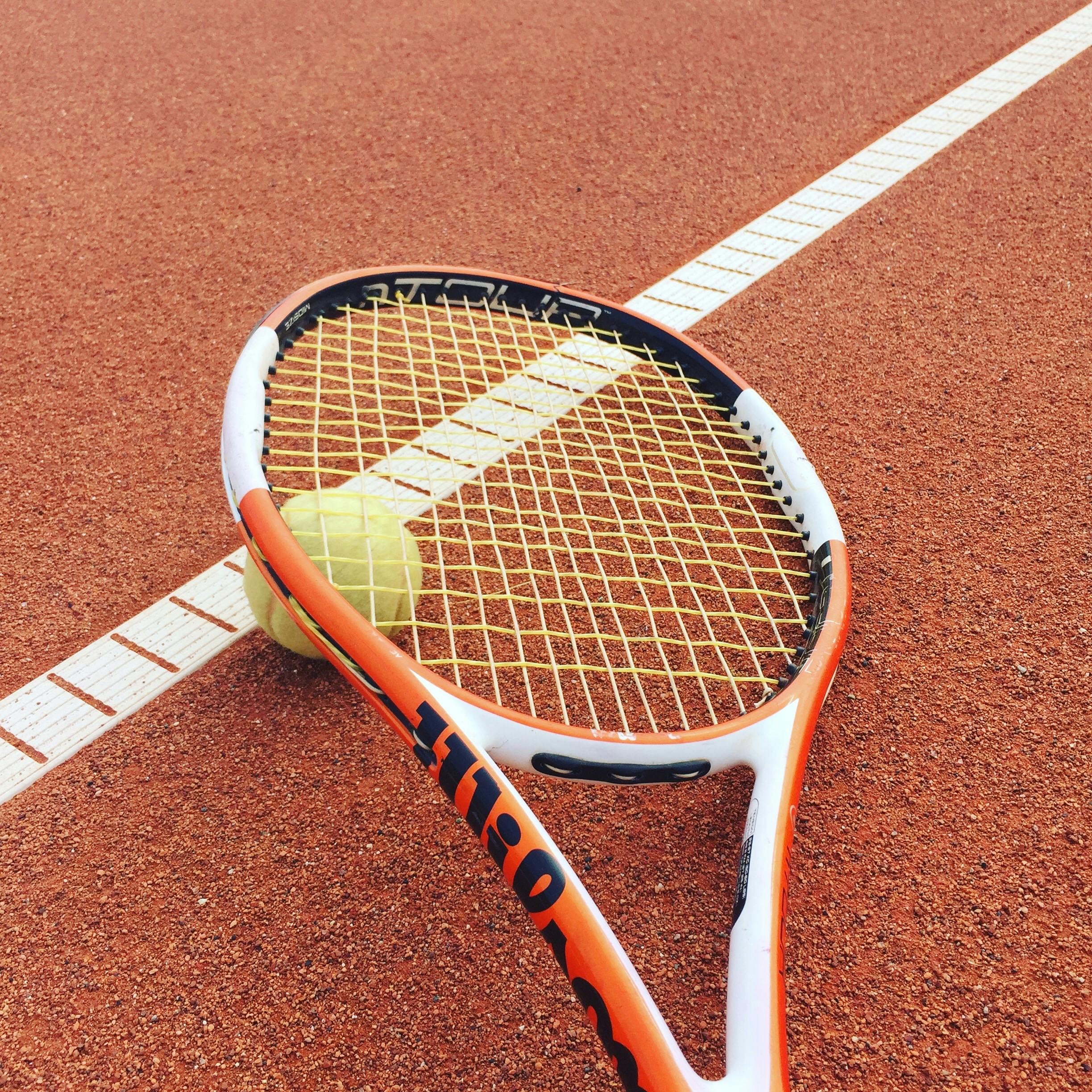Detailed view of a tennis racket and ball on a clay tennis court, perfect for sports enthusiasts.