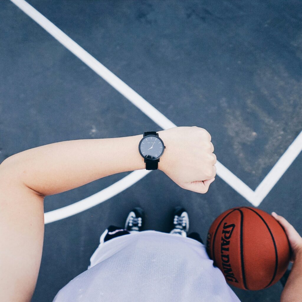 A basketball player checks their wristwatch while holding a ball on an outdoor court.